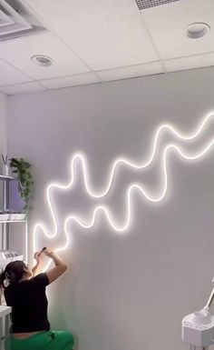 a woman sitting on a chair in front of a white wall with a neon wave painted on it