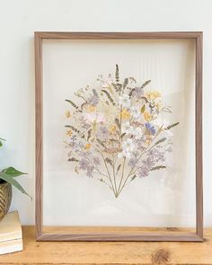 a wooden frame with flowers in it sitting on a shelf next to a potted plant