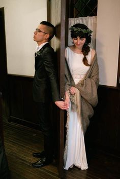 a man standing next to a woman in a white dress and black suit on a wooden floor