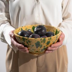 a person holding a yellow bowl filled with plums