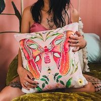 a woman sitting on a bed holding a pillow that has a butterfly painted on it