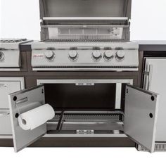 an outdoor kitchen with stainless steel appliances and white counter tops, including the door open to reveal a roll of toilet paper