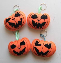 four orange pumpkins with black faces are hanging from key chains on a white surface