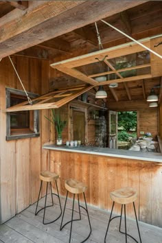 an outdoor bar with three stools in front of it and wood paneling on the walls