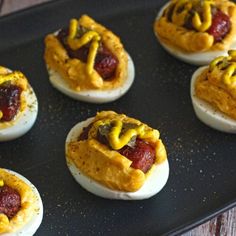 deviled eggs with hotdogs and mustard on them sitting on a black tray