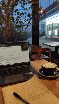 a laptop computer sitting on top of a wooden table next to a cup of coffee