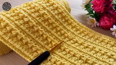 a yellow knitted cloth with a black crochet hook and flowers in the background