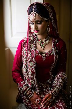 a woman in a red and white wedding outfit is looking down at her hands while wearing jewelry