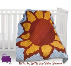 a crocheted sunflower blanket sitting on top of a bed next to a white crib