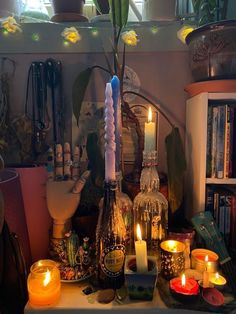 candles and bottles are arranged on a table in front of a bookshelf filled with plants