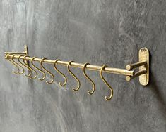 a row of gold hooks hanging on a wall next to a concrete wall with a gray background