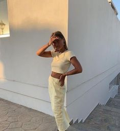 a woman standing in front of a white building with her hand on her head and looking off to the side