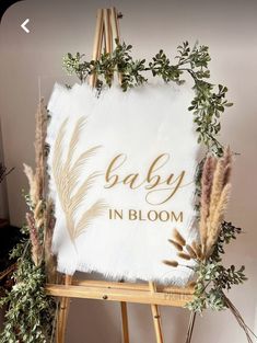 a baby in bloom sign sitting on top of a easel next to some plants