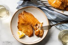 two fish fillets on a white plate with lemon wedges and silverware next to them