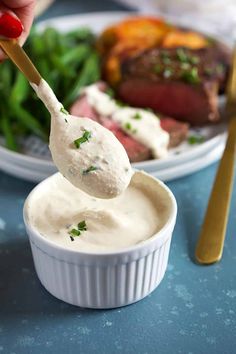 a person dipping some kind of sauce into a small bowl with steak on the side