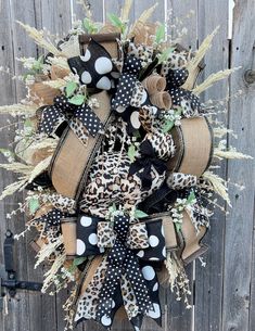 a wreath with black and white polka dots, leopard print bows and green leaves is hanging on a wooden fence