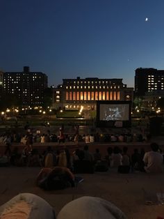 people sitting on the ground in front of a building watching a movie at night time