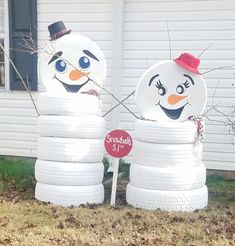 two snowmen standing next to each other in front of a house with tires on the ground