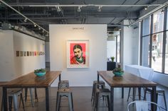 an empty room with tables and stools in front of large windows, paintings on the wall