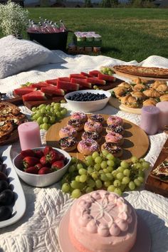 a table filled with lots of food on top of a white blanket next to a field