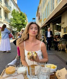 a woman sitting at a table with food in front of her and people walking by