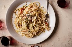 a white plate topped with pasta and sauce next to two glasses of wine on top of a table