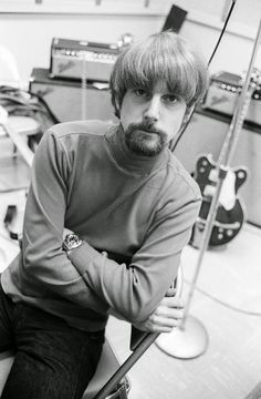 a man sitting on top of a guitar in a room with guitars and other musical equipment