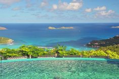 an outdoor swimming pool surrounded by trees and blue water with the ocean in the background