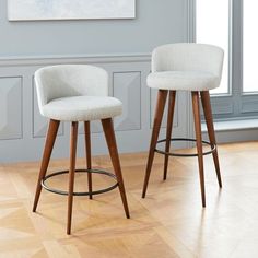 two white bar stools sitting on top of a hard wood floor next to a window