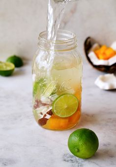 a mason jar filled with lemonade, limes and water being poured into it