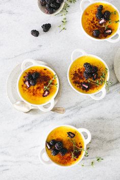 four white bowls filled with soup and garnished with berries, herbs and oregano