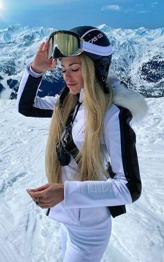 a woman with long blonde hair and goggles standing on top of a snow covered mountain