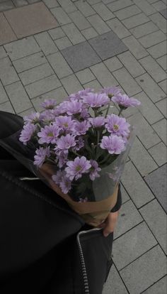 a bouquet of purple flowers is wrapped in a black bag on the sidewalk with a brick walkway behind it