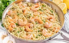 shrimp and pasta in a skillet with lemons, parsley and garlic on the side