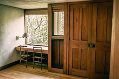 an empty room with two chairs and a desk in front of a window that looks out onto the woods