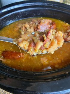 a spoon full of soup with meat and beans in it on top of a black crock pot