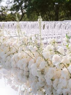 white flowers and greenery are lined up along the edge of an outdoor ceremony aisle