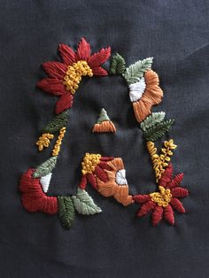 an embroidered letter with flowers and leaves is shown on a piece of black fabric that has been stitched together