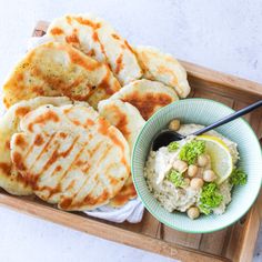 a wooden tray topped with food next to a bowl of hummus