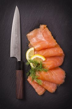 raw salmon with lemon and dill on a black slate board next to a knife