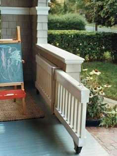 an easel sitting on top of a porch next to a flower bed and potted plant