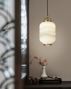 a white vase sitting on top of a table next to a light hanging over it