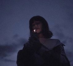 a woman standing in the dark holding a lit candle up to her face and looking into the distance