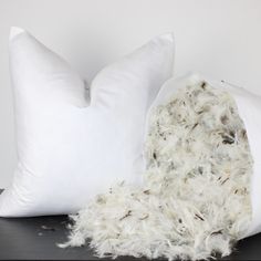 two white pillows sitting next to each other on top of a black table and one is covered in fur