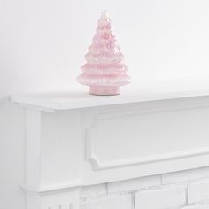 a pink glass christmas tree sitting on top of a white fireplace mantel next to a brick wall