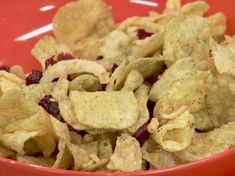 a red bowl filled with corn flakes and cranberry chips on top of a table