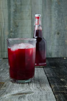 two glasses filled with liquid sitting on top of a wooden table next to a bottle