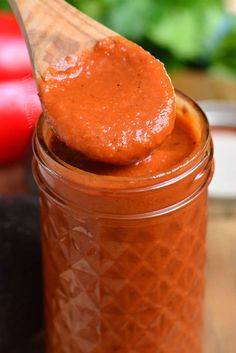 a wooden spoon full of tomato sauce on top of a jar with tomatoes in the background