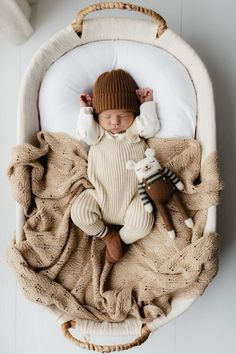 a baby is laying in a crib wearing a hat and holding a stuffed animal