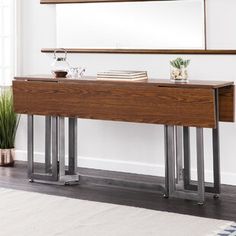 a wooden table with metal legs in front of a mirror and potted plant on top